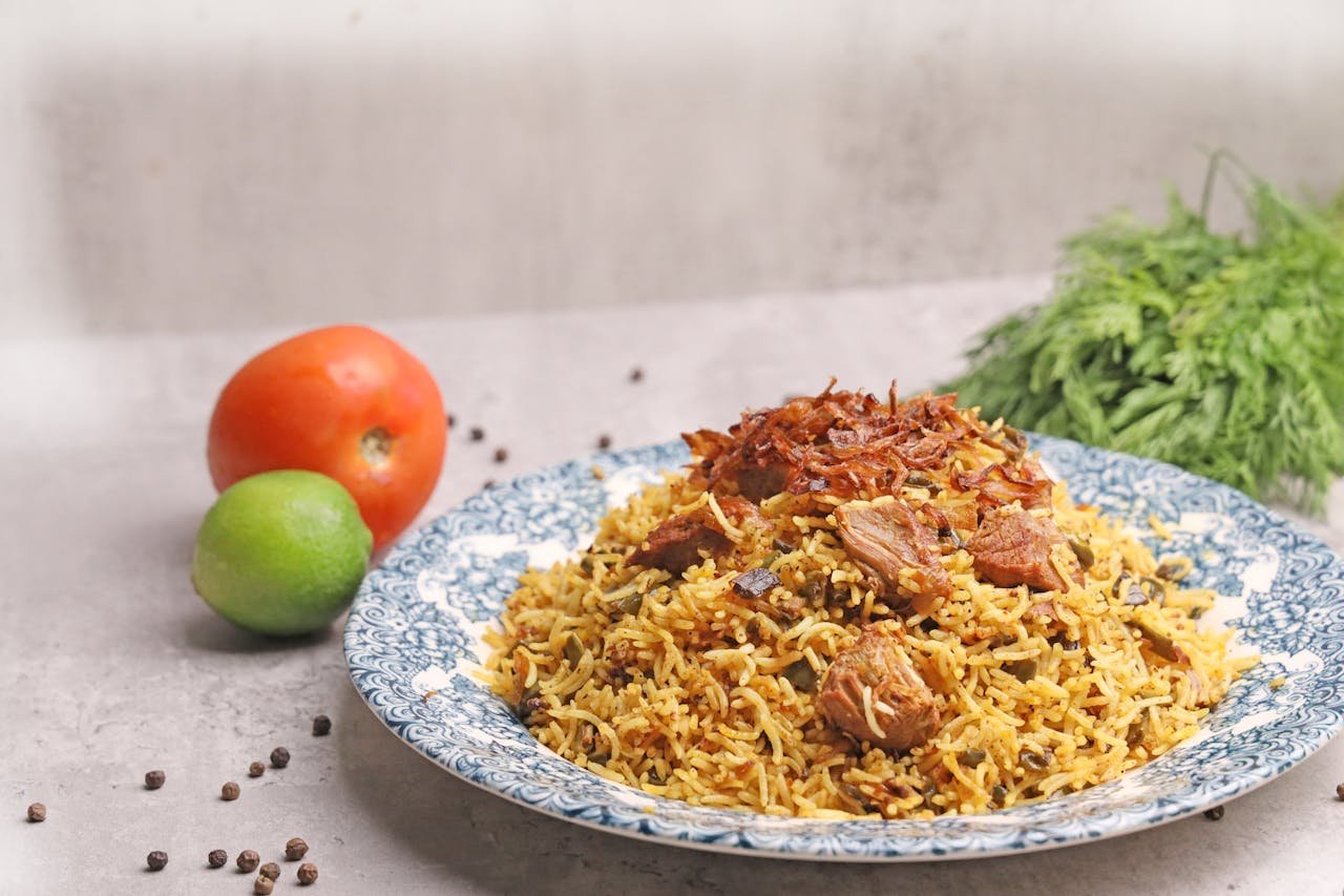 A plate of aromatic biryani with tender meat, surrounded by fresh vegetables, ready to enjoy.