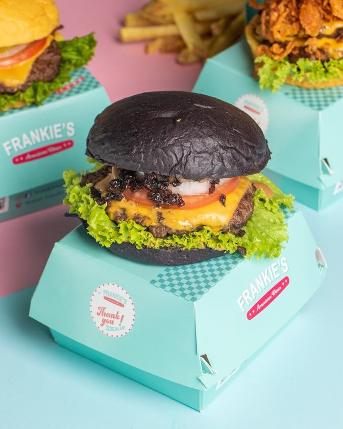 Juicy gourmet burger with a distinctive black charcoal bun served in stylish packaging, perfect for food lovers.
